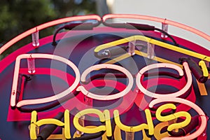 A red and yellow neon sign that reads Ã¢â¬ÅDog HausÃ¢â¬Â on the side of a white buildings surrounded by lush green trees in Pasadena photo